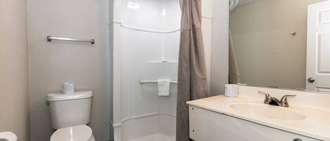 A bathroom with a toilet, a shower, and a sink with a mirror.