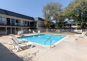 A swimming pool with lounge chairs, a fenced area, and a building with multiple balconies. - Lubbock Inn & Suites (Lubbock)