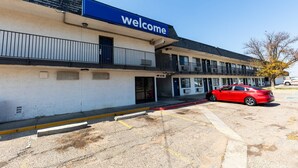 A building with a 'Welcome' sign, a red car parked in front, and a clear sky.