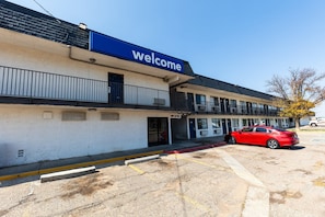 A building with a 'Welcome' sign, a red car parked in front, and a clear sky.