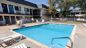 A rectangular swimming pool with a metal ladder, surrounded by white lounge chairs and a fenced area.
