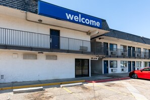 Un edificio con un letrero de 'Welcome', un estacionamiento y un coche rojo estacionado al frente.