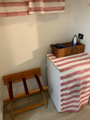 A small room with a wooden bench, a white radiator, and a wooden box containing an iron and a bottle.