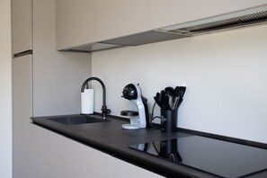 A modern kitchen with a black countertop, a white sink, and a coffee maker. - GuestHost - Cozy Apartment with Parking (Venturelli-Fenili)