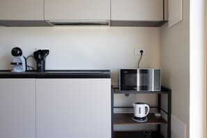A kitchenette with a microwave, kettle, and a coffee maker on a shelf. - GuestHost - Cozy Apartment with Parking (Venturelli-Fenili)