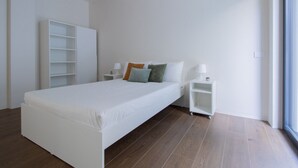 Une chambre à coucher au style minimaliste, avec un lit simple, des tables de chevet, une armoire et une fenêtre.