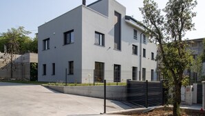 Un immeuble moderne à plusieurs étages, doté d’un toit plat, de fenêtres rectangulaires et d’une entrée fermée par un portail.