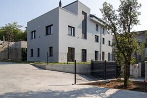 A modern multi-story building with a flat roof, rectangular windows, and a gated entrance. - GuestHost - Cozy Apartment with Parking (Venturelli-Fenili)