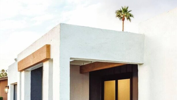 A modern building with a flat roof, a covered outdoor seating area with two wicker chairs, and a palm tree in the background. - LUXE - SOTO Luxury House in Old Town Scottsdale (Scottsdale)