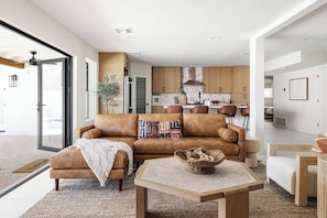 Ein modernes Wohnzimmer mit Ledersofa, Couchtisch und einer Küche im Hintergrund.