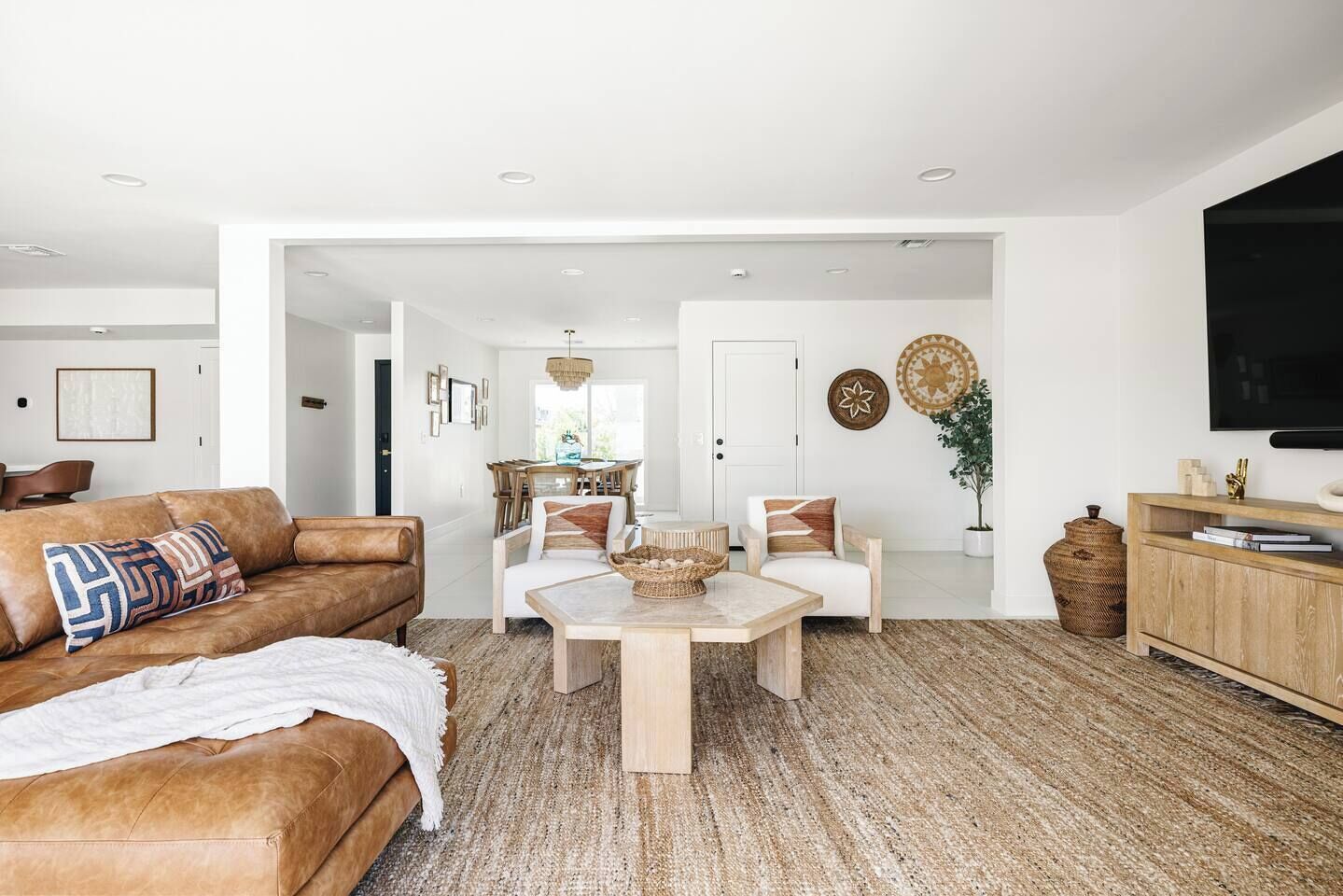 Een ruime woonkamer met een bruine leren bank, een houten salontafel en een eethoek met een houten tafel en stoelen.