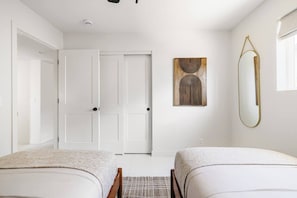 Ein Hotelzimmer mit zwei Betten, einer Tür, einem Wandspiegel und einem abstrakten Kunstwerk.