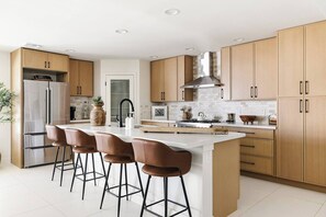 A modern kitchen with a central island, bar stools, stainless steel appliances, and wooden cabinetry. - SOTO: Scottsdale Home, Pool, Spa & Putting Green (Scottsdale)