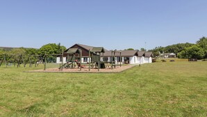 A playground with swings and climbing structures, a building with a brown roof, and a grassy field. - 7 Brunston Avenue (Girvan)