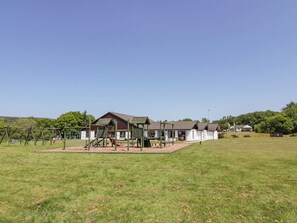A playground with swings and climbing structures, a building with a brown roof, and a grassy field. - 7 Brunston Avenue (Girvan)