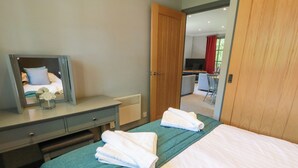 A hotel room with a bed, a desk with a mirror, a chair, and a view of a dining area through an open door. - 7 Brunston Avenue (Girvan)