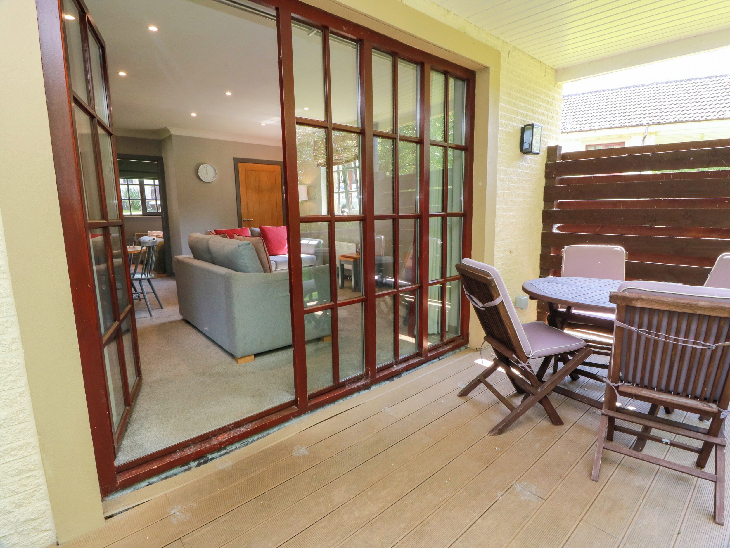 A patio area with a wooden table and chairs, a sliding glass door leading to an indoor living space, and a clock on the wall.