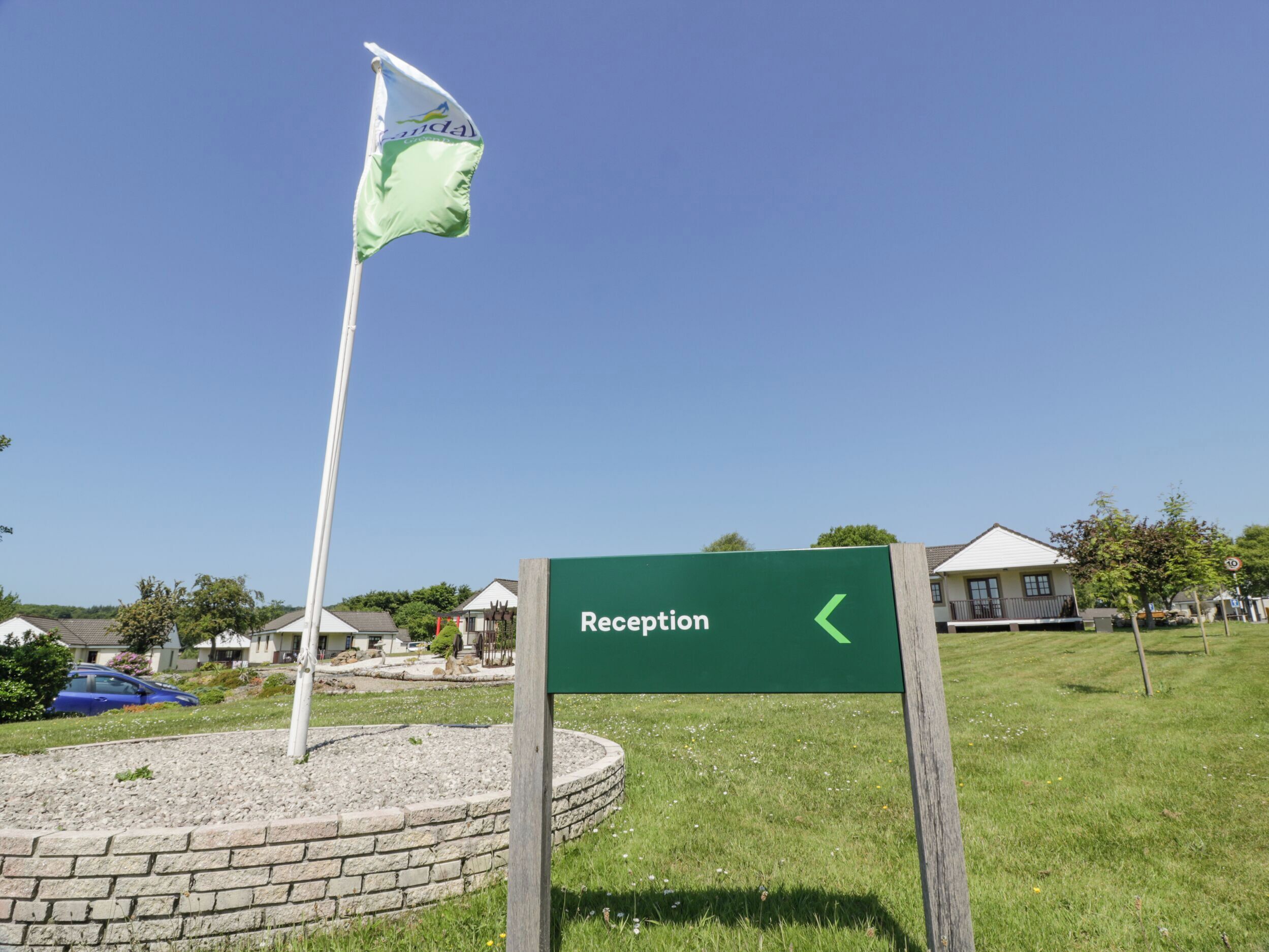 A reception sign with a directional arrow, a flagpole with a flag, and a brick circular area with a grassy field.