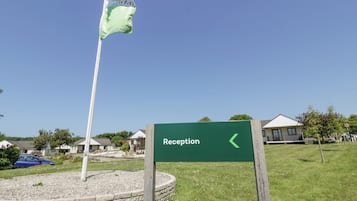 A reception sign with a directional arrow, a flagpole with a flag, and a brick circular area with a grassy field.