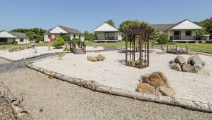 A row of single-story cottages with a gravel courtyard, a wooden bridge, and a pergola. - 7 Brunston Avenue (Girvan)
