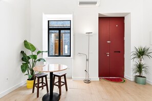 A room with a round table, two chairs, a potted plant, a red door, and a window with a view of a building. - GuestReady-Charming Aveiro Home (Aveiro)