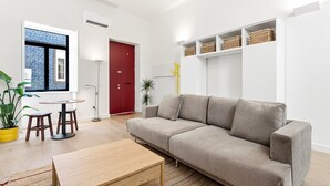 A modern living room with a sofa, a coffee table, a small dining table, and chairs. There is a red door, a potted plant, and a shelf with baskets. - GuestReady-Charming Aveiro Home (Aveiro)