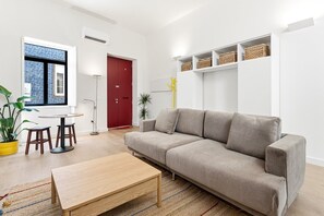 A modern living room with a sofa, a coffee table, a small dining table, and chairs. There is a red door, a potted plant, and a shelf with baskets. - GuestReady-Charming Aveiro Home (Aveiro)