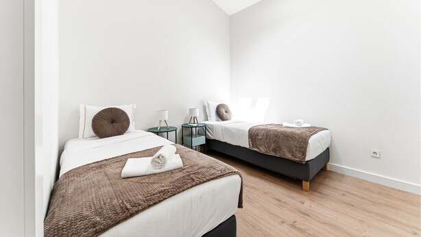 A modern bedroom with two beds, each with a bedside table and lamp, and a skylight above. - GuestReady-Charming Aveiro Home (Aveiro)
