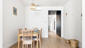 A dining area with a wooden table and chairs, a hanging light fixture, and a hallway leading to another room. - GuestReady-Charming Aveiro Home (Aveiro)