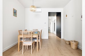 A dining area with a wooden table and chairs, a hanging light fixture, and a hallway leading to another room. - GuestReady-Charming Aveiro Home (Aveiro)