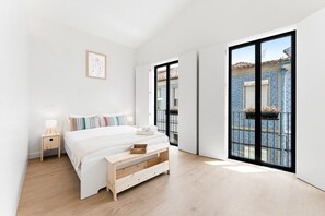 A minimalist bedroom with a bed, bedside table, and a view of a blue-tiled building through large windows. - GuestReady-Charming Aveiro Home (Aveiro)