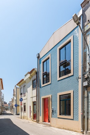 A street view with buildings featuring blue and beige facades, a red door, and a clear sky. - GuestReady-Charming Aveiro Home (Aveiro)