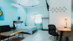 A room with a bed, a desk, a chair, a bench, and a hanging light fixture.