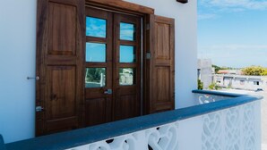 A wooden door with glass panels, a balcony with a white railing, and a clear sky in the background.