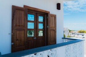 A wooden door with glass panels, a balcony with a white railing, and a clear sky in the background.