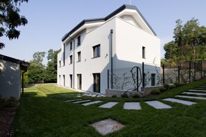 A modern two-story building with a flat roof, a symmetrical facade, and a well-maintained lawn with stepping stones leading to the entrance. - GuestHost - Lovely Apartment with Parking (Venturelli-Fenili)