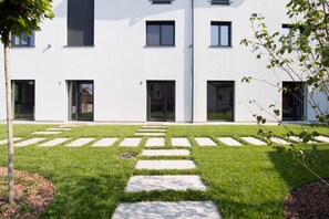 Un bâtiment moderne doté d’un toit plat, de fenêtres rectangulaires et d’une cour pavée avec des dalles formant un chemin.
