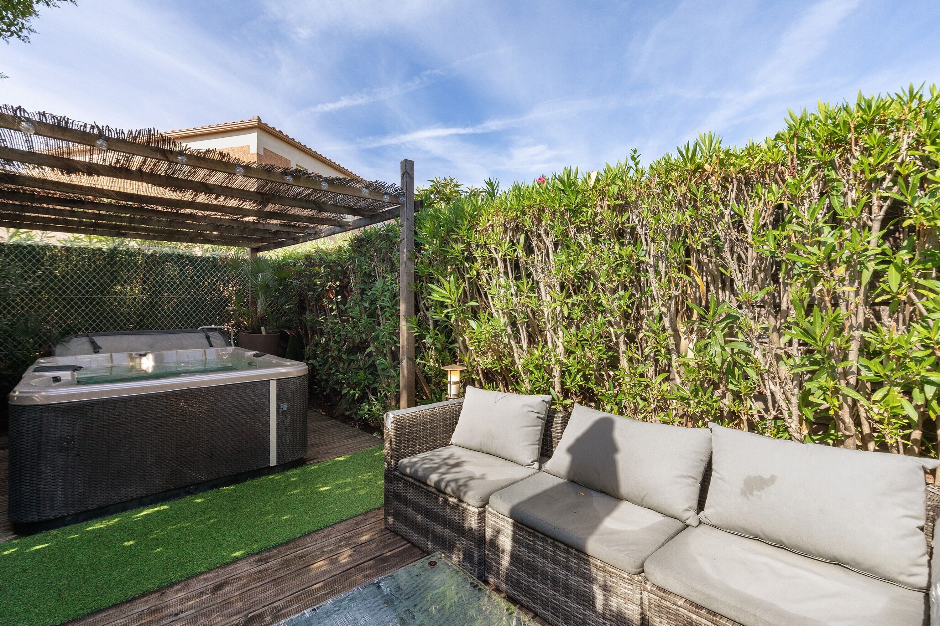 A hot tub, a wicker sofa, and a wooden pergola in a backyard.