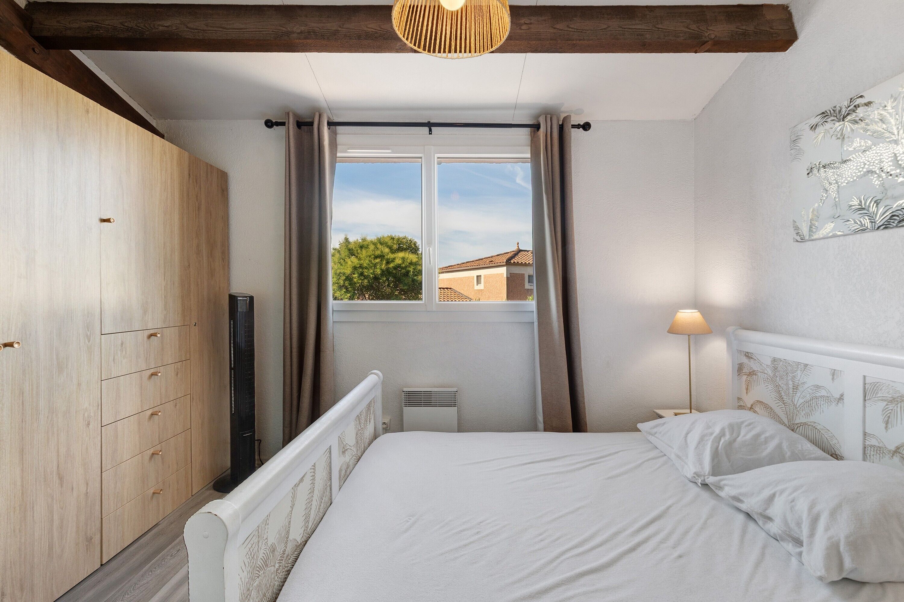 A bedroom with a bed, a wardrobe, a window with curtains, a radiator, and a wall-mounted lamp.