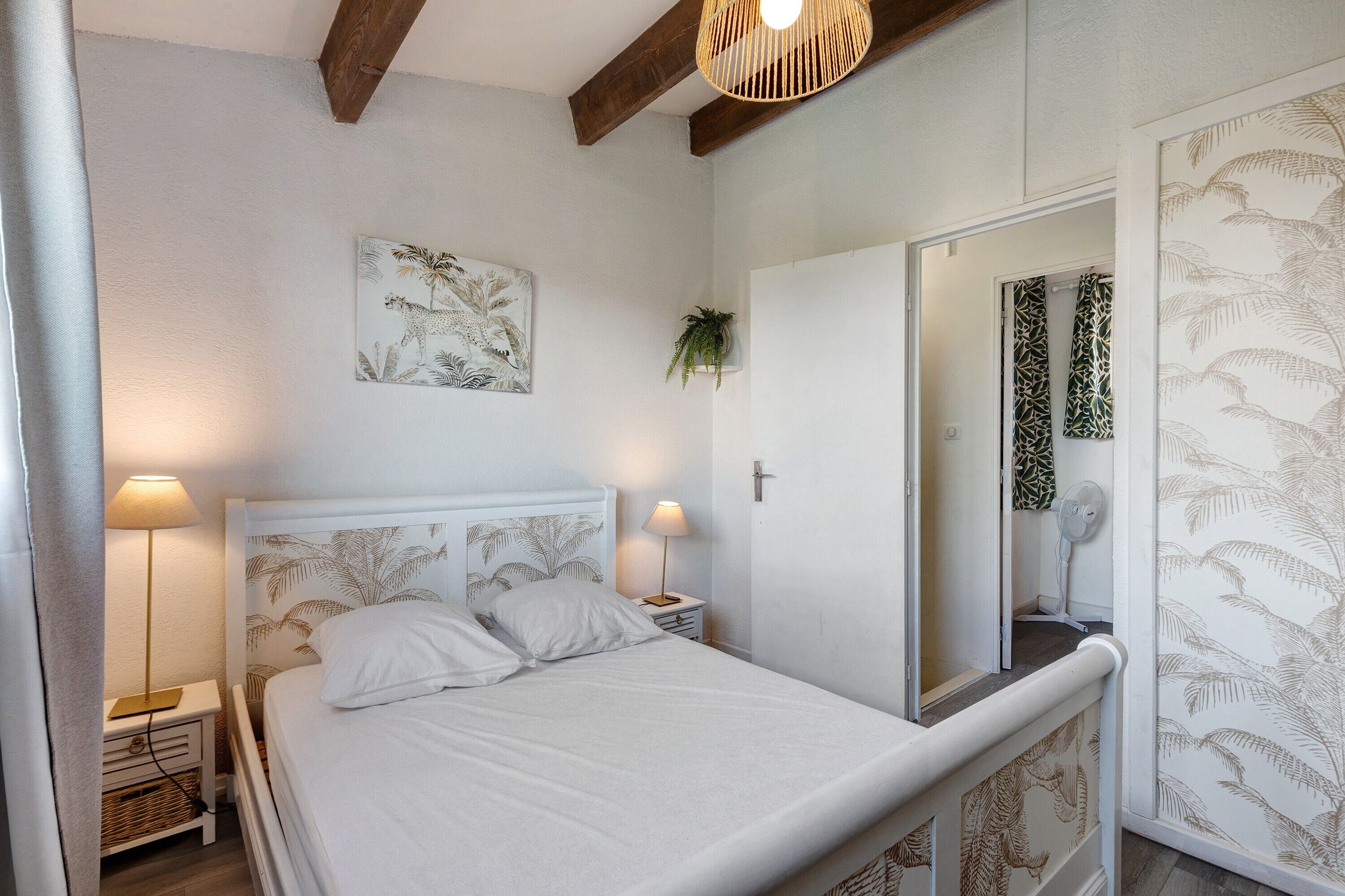 A bedroom with a bed, bedside lamps, a wall-mounted plant, and a mirror with a patterned curtain.