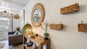 A modern living room with a grey sofa, a wooden console table with decorative items, a large woven mirror, and woven wall hangings.
