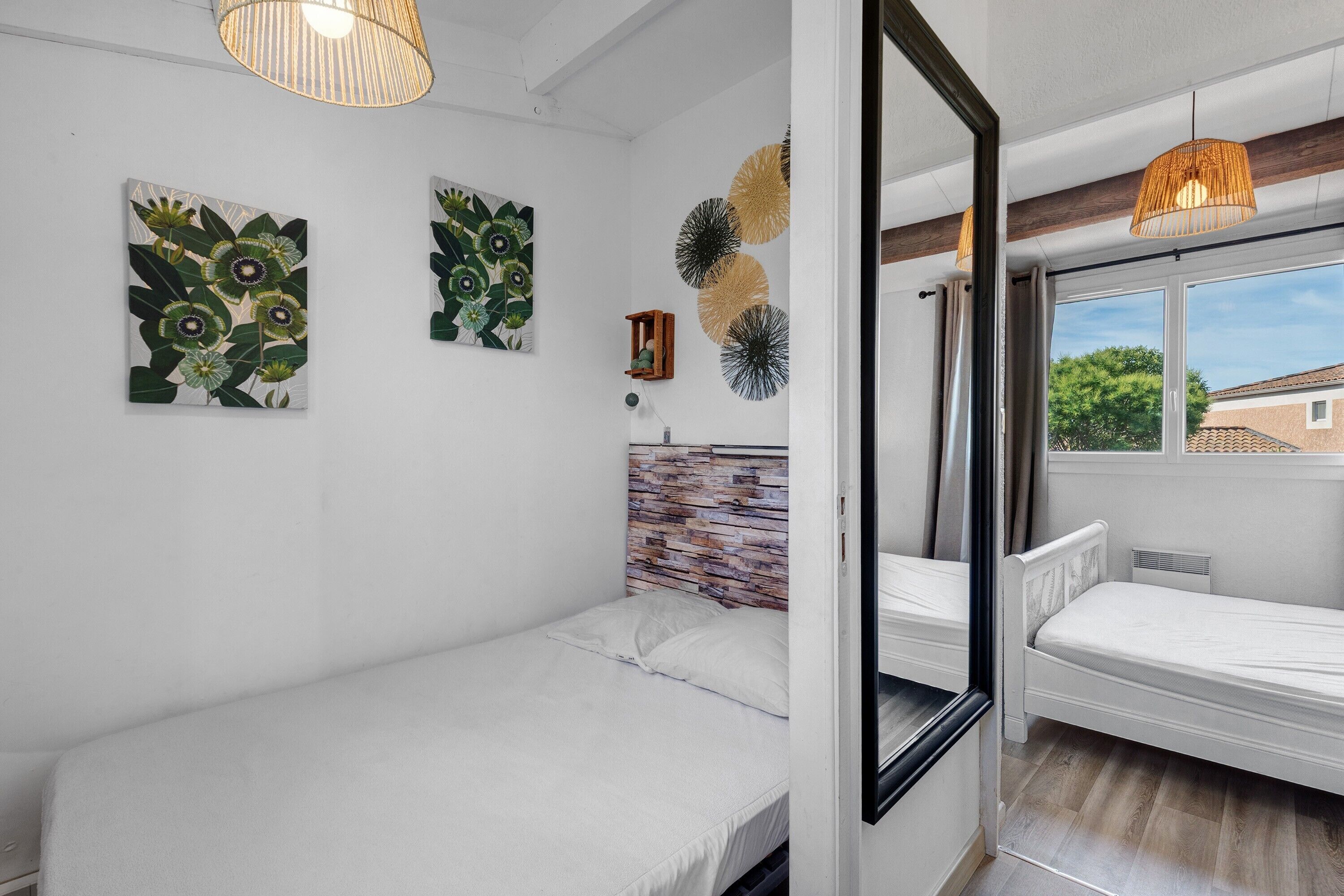 Un dormitorio con cama, mesita de noche, espejo y ventana.