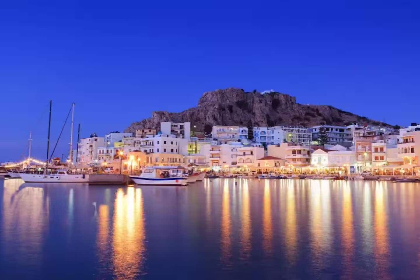 A coastal town at dusk with buildings along the waterfront and boats docked.