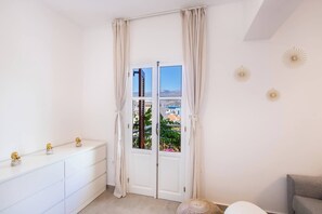 A room with a white dresser, a grey sofa, and a view through a door. - Unique Suite (Karpathos)