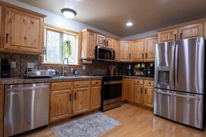 A kitchen with wooden cabinets, stainless steel appliances, granite countertops, and a window with a view of trees. - Rev & Rest Lodge Duck Creek (Duck Creek Village)