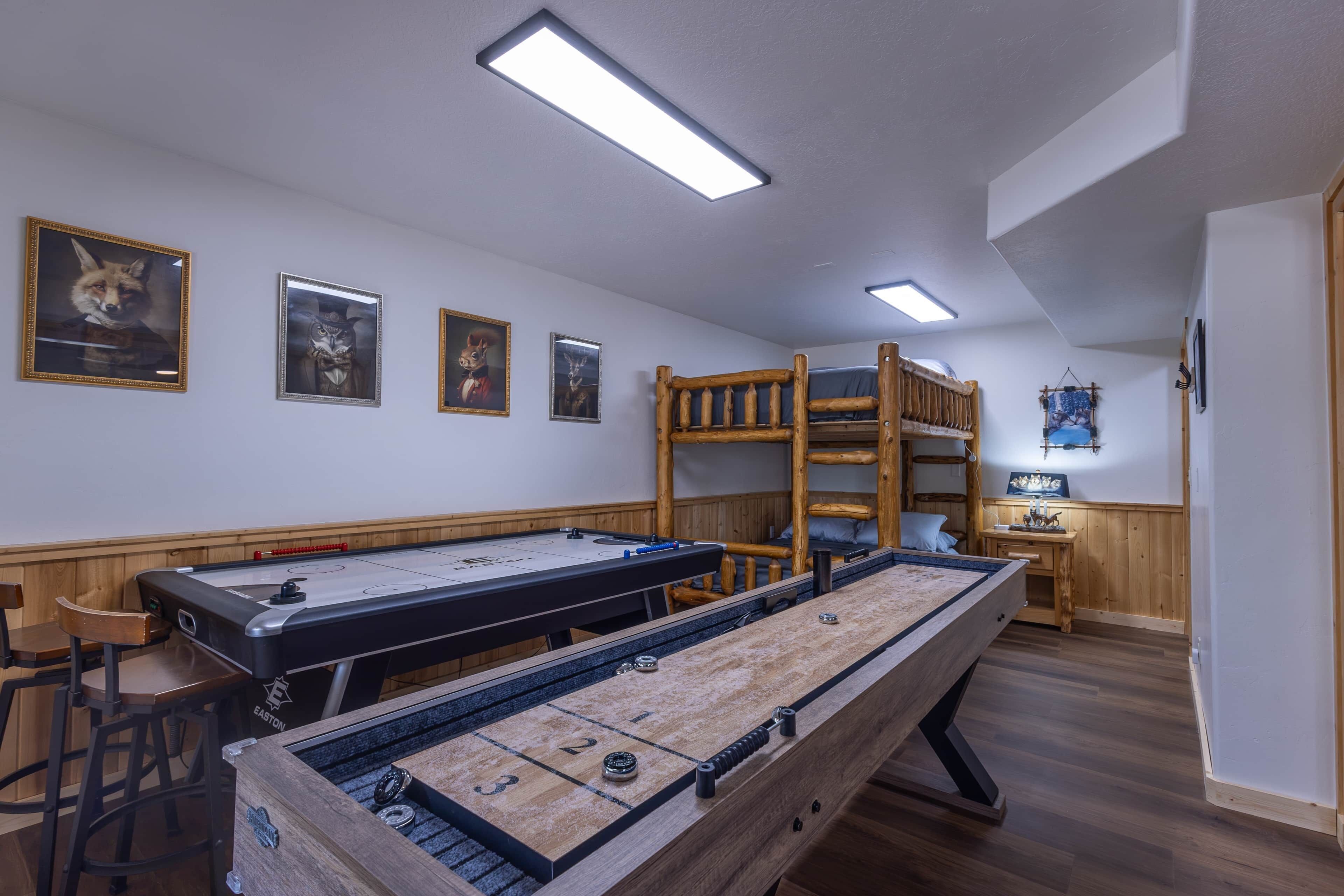 A room with a shuffleboard table, a pool table, bunk beds, and framed artwork on the walls.