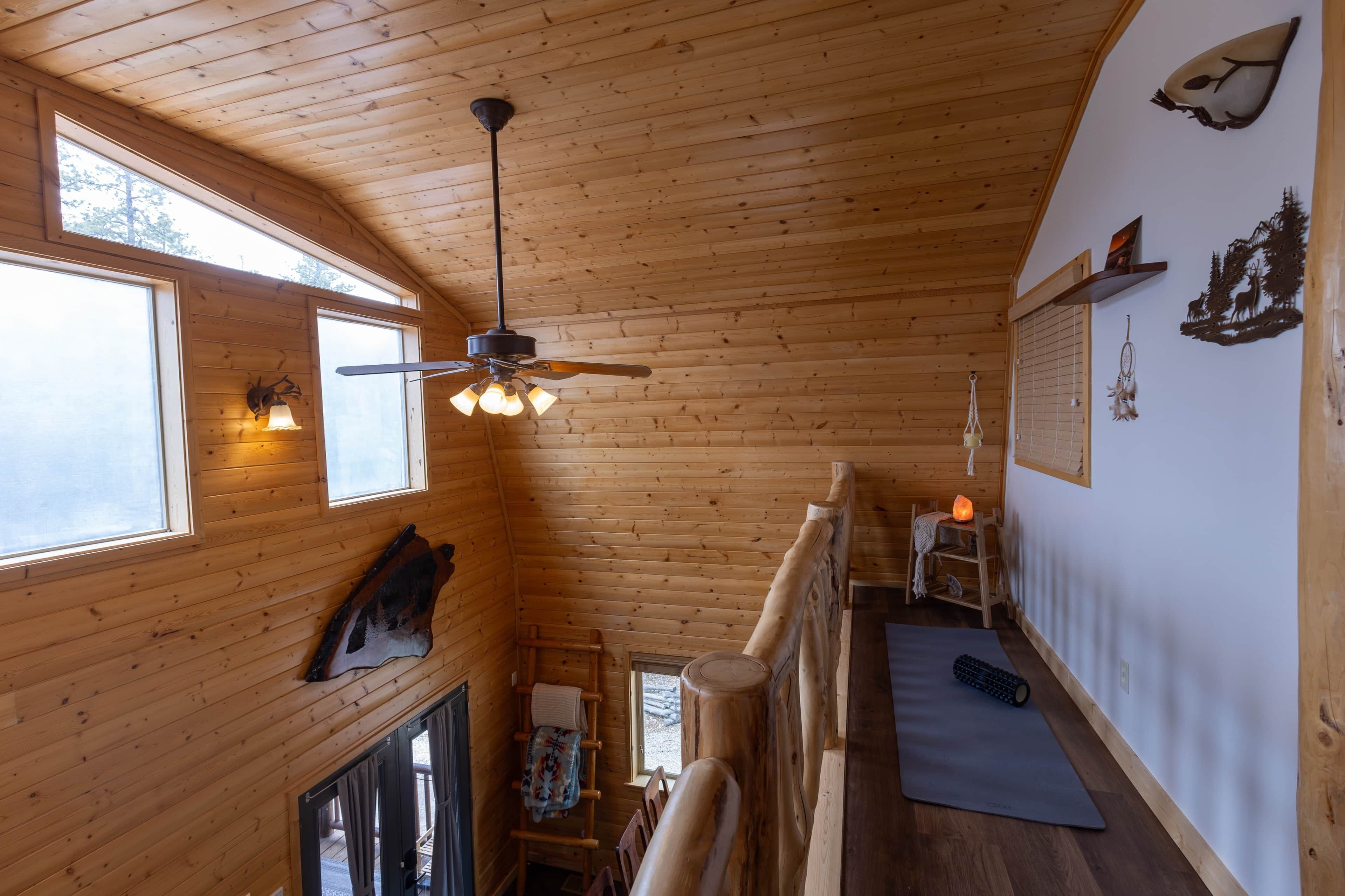 Ein Holzinnenraum mit Deckenventilator, Fenstern, Kamin, Yogamatte und Wandgestaltungen.