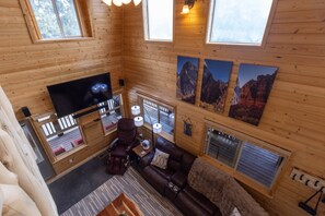 Interior d'una cabana de fusta amb televisió de pantalla plana, sofà de cuir i quadres de paisatges de muntanya.