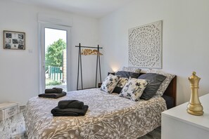 A bedroom with a bed, pillows, a bedside table, a nightstand, a wall-mounted artwork, and a door leading to an outdoor area. - Holiday Home 'Gîte du Bord de Mer' with Wi-Fi and Air Conditioning (Avrillé)