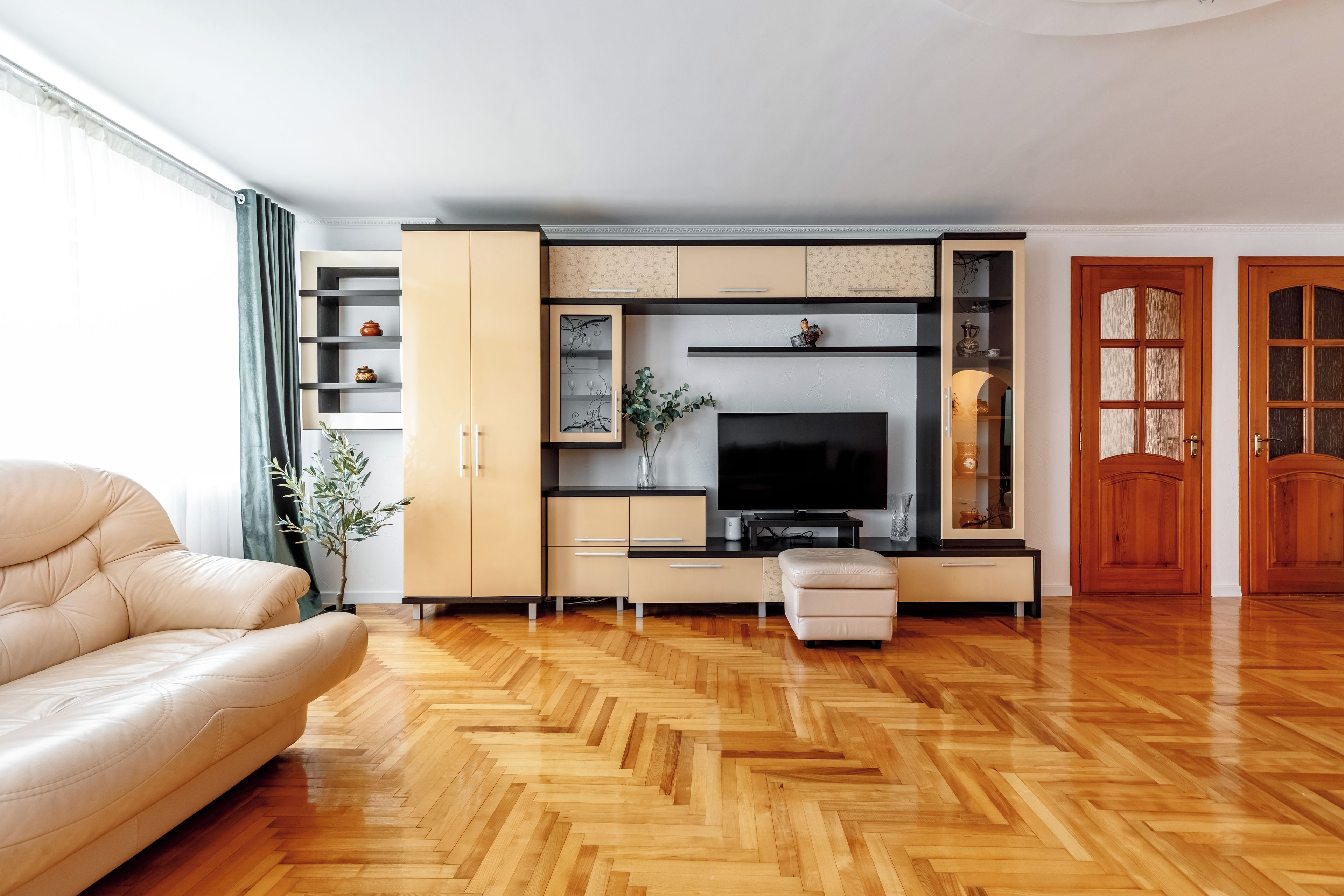 A modern living room with a sofa, TV, wooden herringbone floor, and built-in shelving.